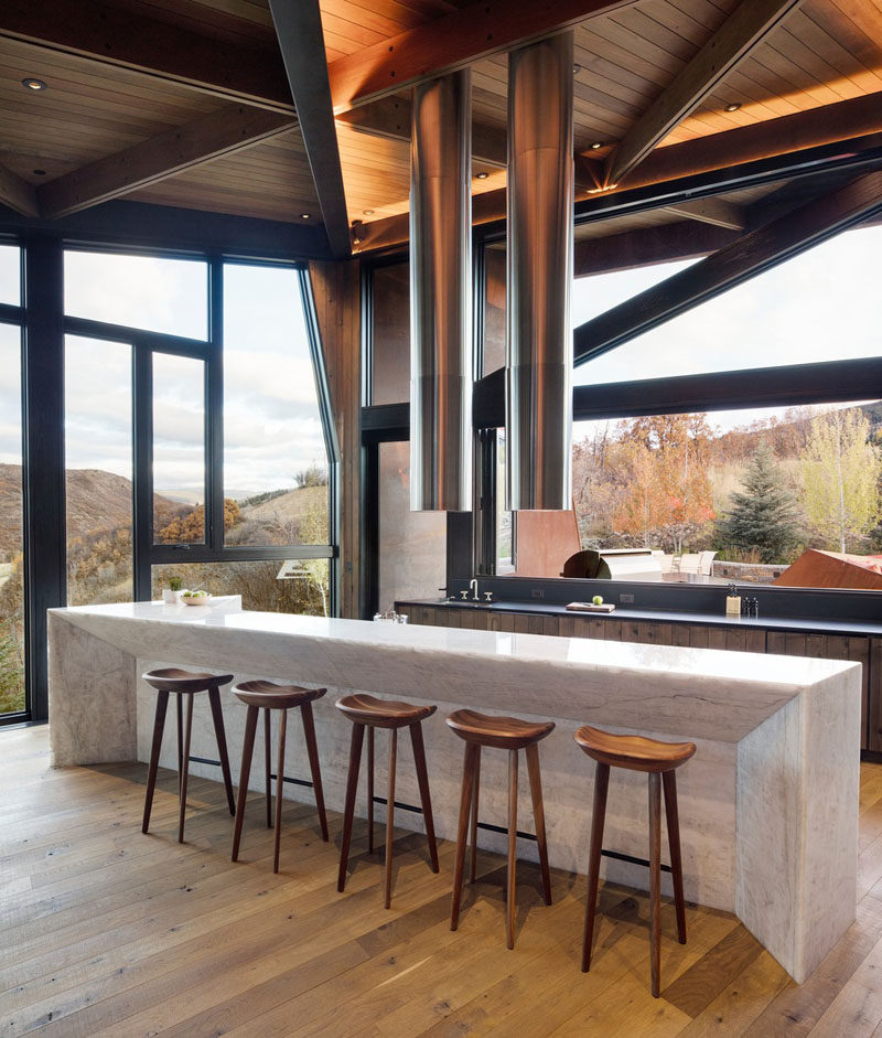 This large kitchen creates a place for gatherings, while a large light-colored island provides a place for seating, and the large black-framed windows flood the interior with natural light. #KitchenDesign #ModernKitchen #Windows