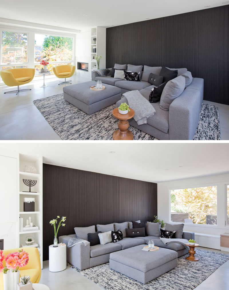 In this modern living room, a dark wood slat wall provides a backdrop for the comfortable grey couch, while large windows on either side of the living room provide views of the front and back yards. #LivingRoom #DarkAccentWall