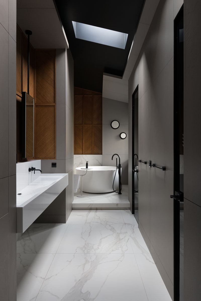 In this modern master bathroom, a round freestanding bathtub has been placed on a raised platform, while a skylight draws the eye upwards to the high ceiling. #MasterBathroom #BathroomDesign #RoundBath