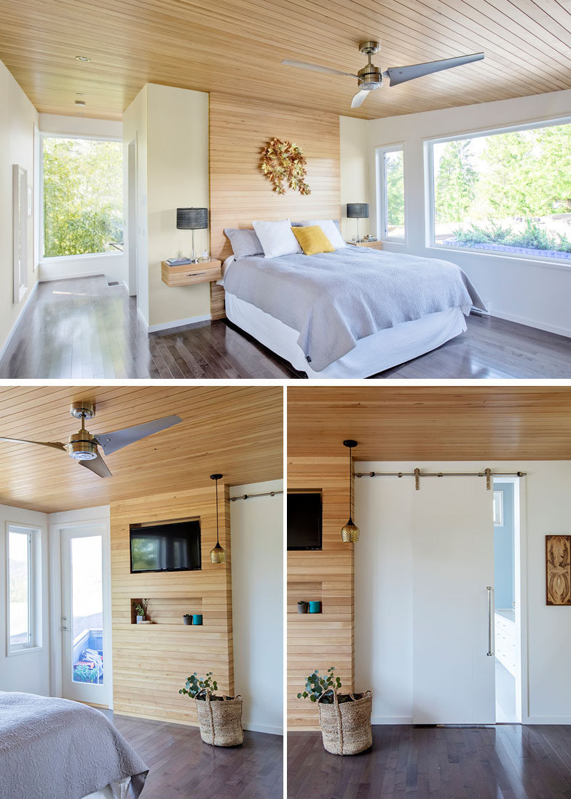 The light wood used on the ceiling of this modern bedroom, has also been used to create an accent wall behind the bed, while wood bedside tables float on either side of the bed. Opposite the bed is a smaller wood accent wall that surrounds a television, and a sliding barn door hides the master bathroom. #ModernMasterBedroom #WoodAccentWall #WoodCeiling