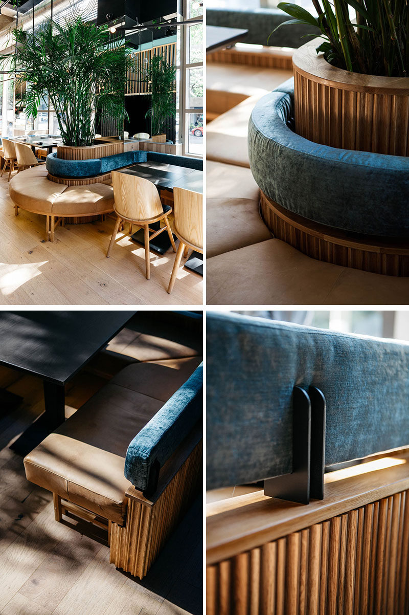 This modern restaurant features curved banquette seating that wraps around planters with tall plants, that are reflected in the mirror on the wall. #Banquette #RestaurantDesign ModernRestaurant