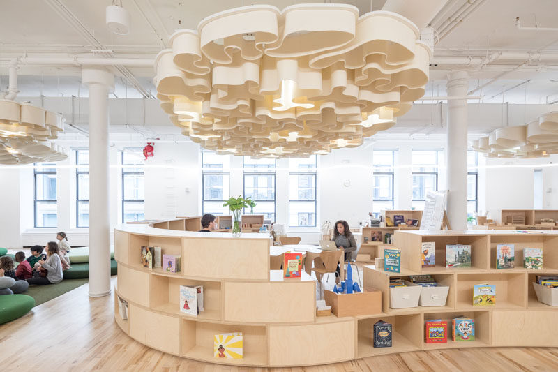 In this modern school, acoustic clouds, hanging from the ceiling and made of felt, reflect the different patterns in nature – fingerprint, coral, landscape and moon – and illuminate with Ketra bulbs that shift in color and intensity based on the time of day. #AcousticClouds #ModernSchool #CurvedShelving