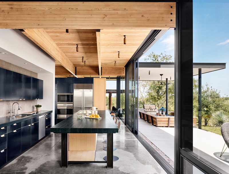 Large sliding glass doors open this modern kitchen with black steel cabinetry, to the patio, where there's a bbq and covered lounge area. #Kitchen #KitchenDesign #ModernKitchen