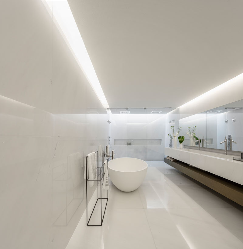 In this modern master bathroom, a glass shower screen separates the shower from the rest of the bathroom, while a freestanding bathtub sits opposite the vanity. #MasterBathroom #BathroomDesign #WhiteBathroom