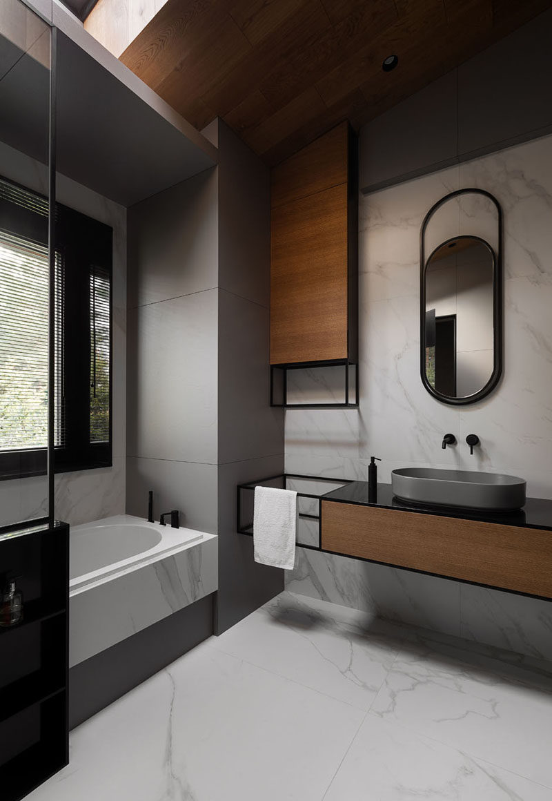 In this modern grey, black, and wood bathroom, curved elements like the mirror and the basin reflect the curved interior shape of the bath. #ModernBathroom #BathroomDesign