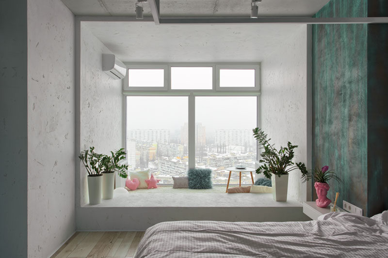 This modern bedroom features a small nook area by the windows, that's been decorated with pillows, a soft carpet, and a small table. #WindowNook #ReadingNook #BedroomDesign