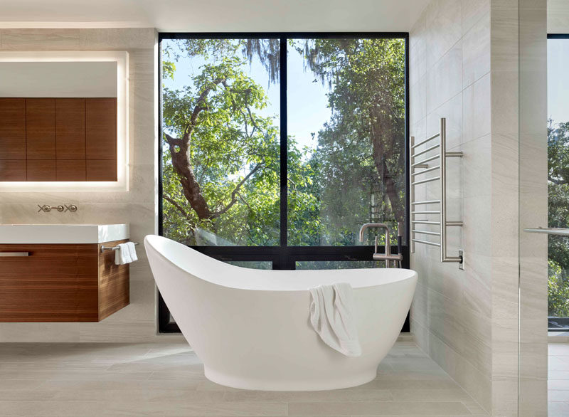 In this modern master bathroom, a curved freestanding bathtub is positioned in front of the windows to take in the tree views. #MasterBathroom #BathroomDesign