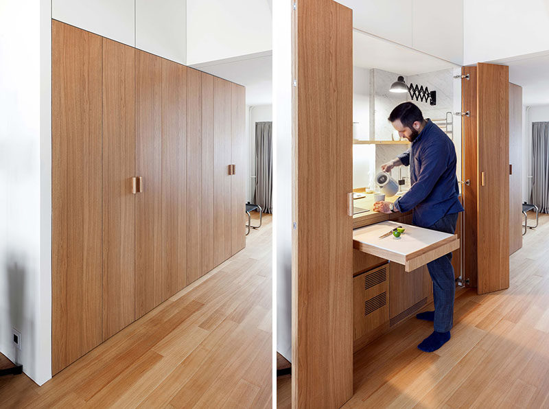 This small and modern apartment hides the kitchen, storage, and a laundry within a wood closet in the hallway. #InteriorDesign #SmallKitchen #HiddenKitchen #HiddenLaundry