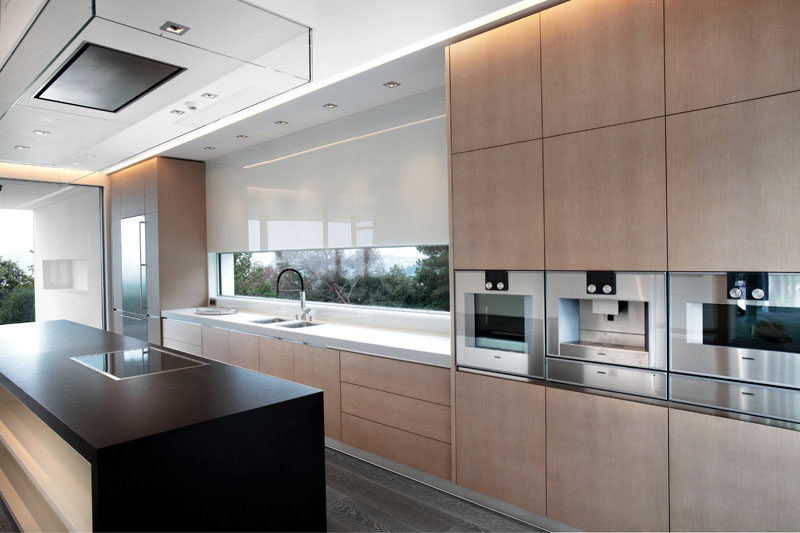 In this modern kitchen, light minimalist wood cabinets have been paired with both a white countertop and a black kitchen island. #KitchenDesign #ModernKitchen