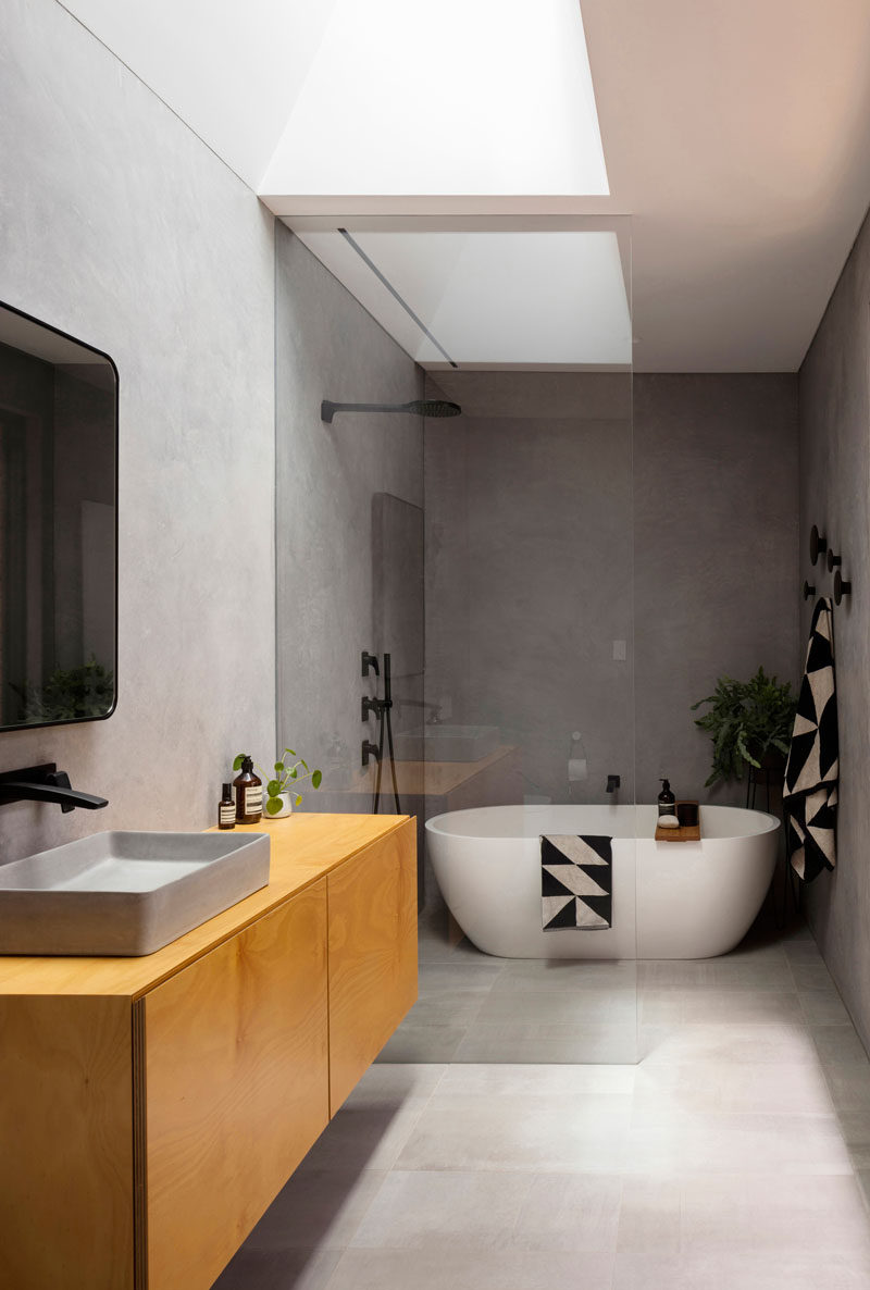 In this modern bathroom, there's a skylight adding natural light, while a glass partition separates the shower and bath from the rest of the room. #ModernBathroom #BathroomDesign #BathroomLayout