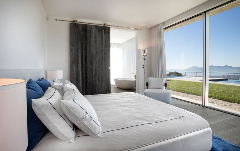 This contemporary bedroom has floor-to-ceiling windows that provide views of the backyard, swimming pool, and distant mountains. #BedroomDesign #Windows