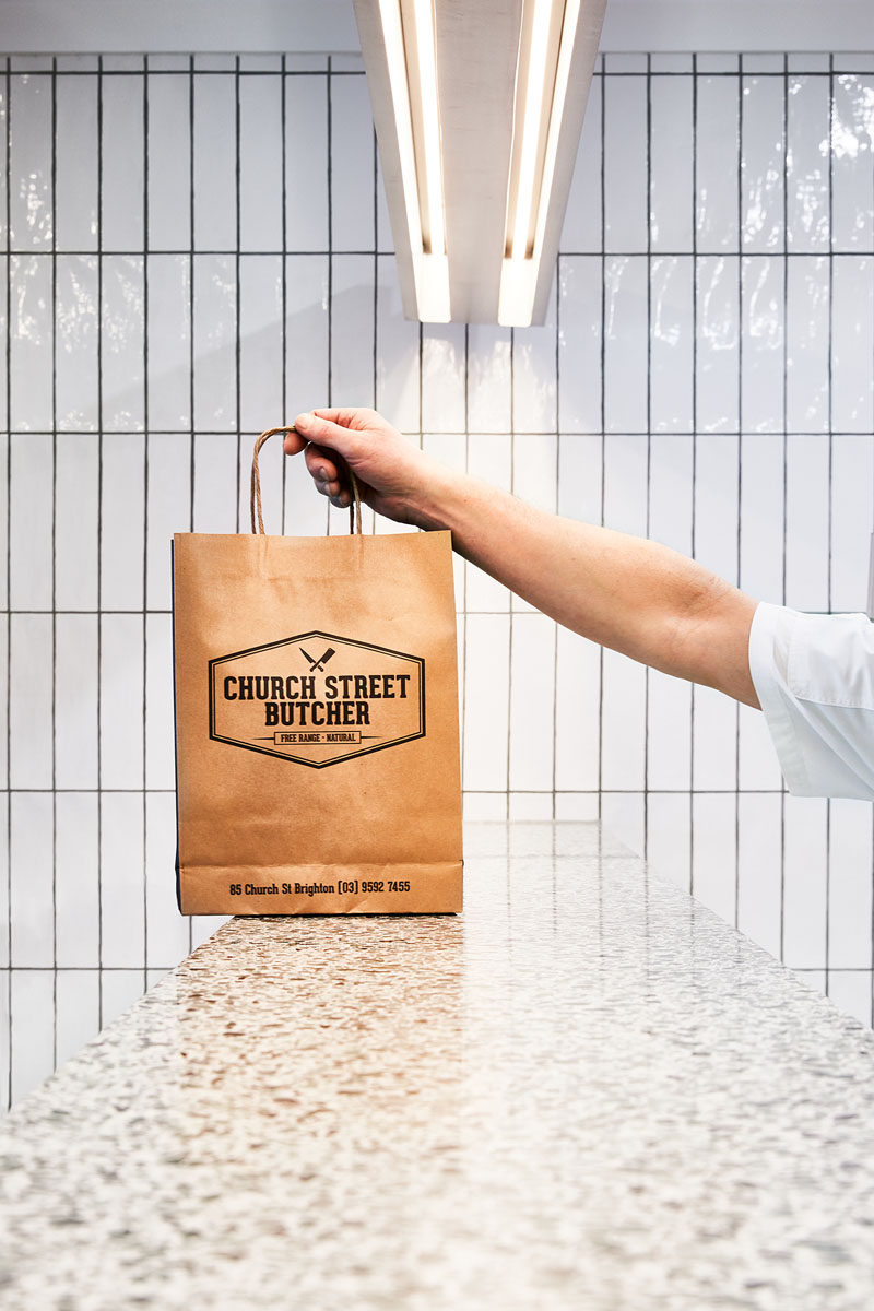 In this modern butcher, white rectangular tiles with dark grout cover the walls, and the service counter is made from a Terrazzo slab. #ModernRetail #ModernButcher #InteriorDesign #RetailDesign