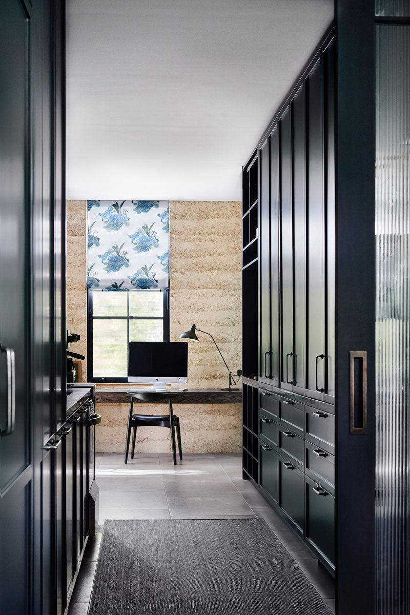 In this modern house, dark cabinetry lines a hallway that leads to a home office, with a desk positioned in front of the window. #DarkCabinets #HomeOffice