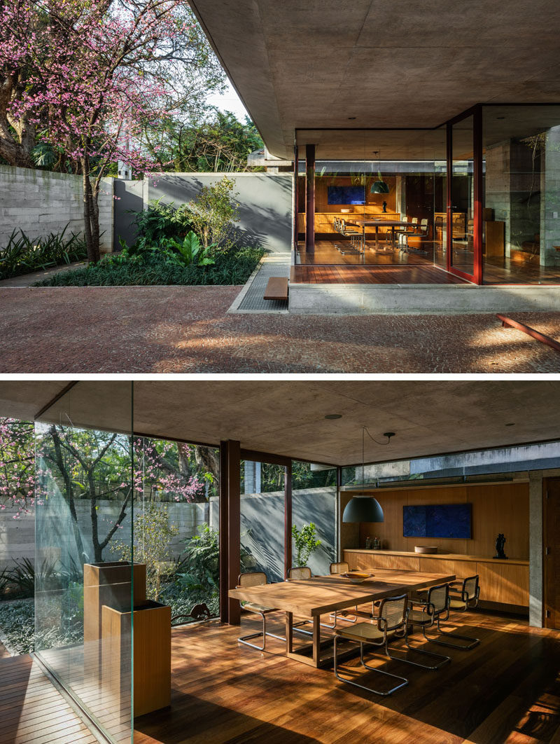 Located at the front of this modern house is the dining room and kitchen, both of which are slightly elevated relative to the sidewalk. Glass walls allow an abundance of natural light to filter through to the interior, and provide views of the gardens. #DiningRoom #GlassWalls