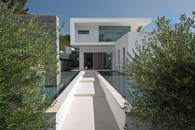 Water features line the path to the front door, while stone accents and plants contrast the white exterior of the house. #Landscaping #WaterFeature #ModernArchitecture