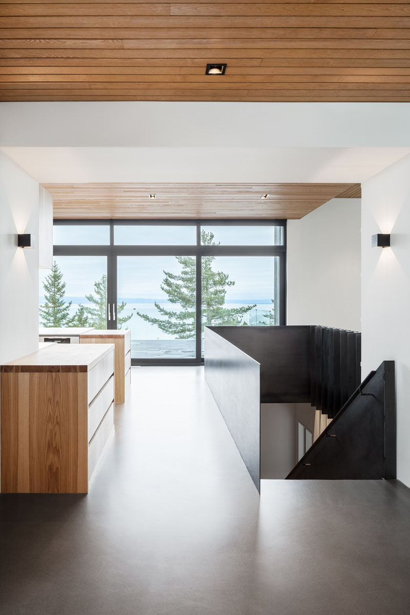 The entryway of this modern house has concrete floors and wood ceilings, and opens up to the main floor with the living room, kitchen, and dining room. #Entryway #WoodCeiling #ConcreteFloors