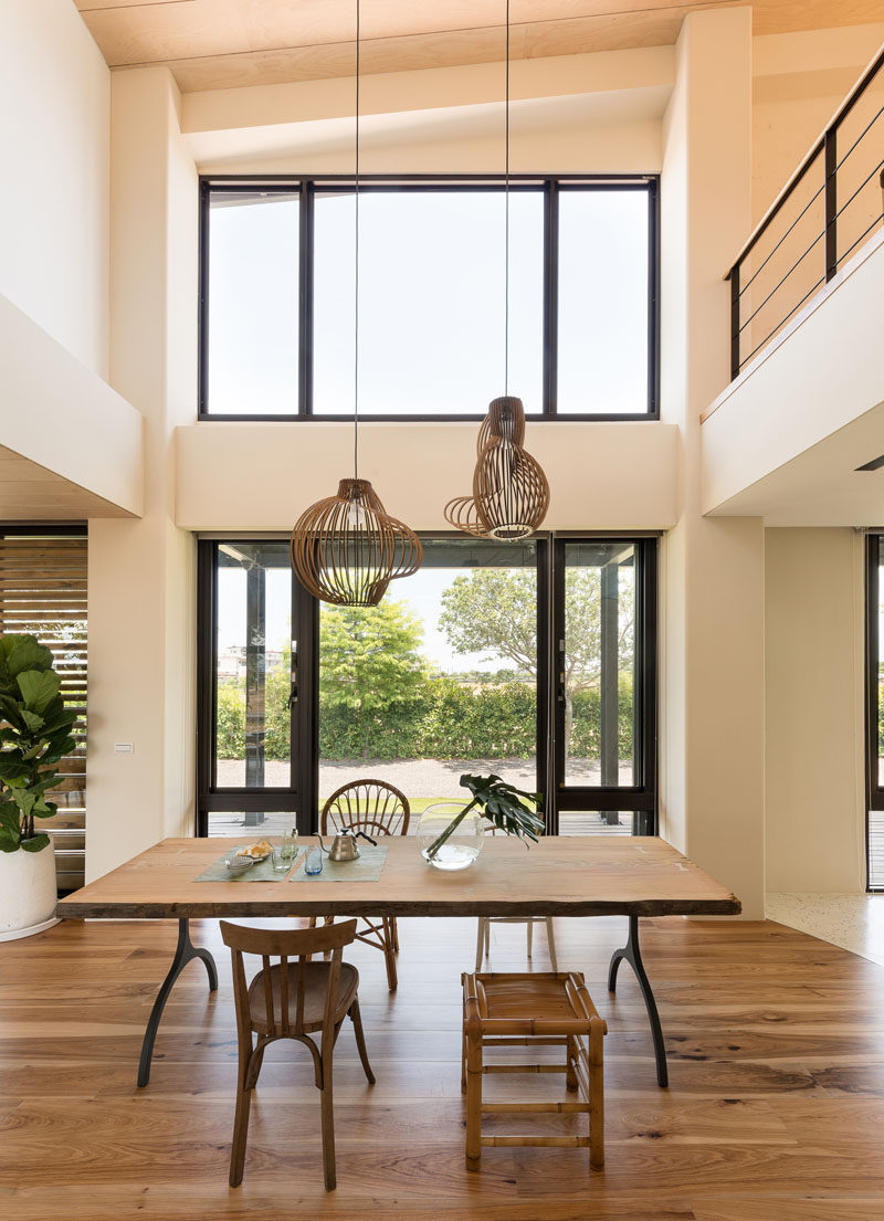 In this open dining area, a simple wood dining table is surrounded by different styles of seating, while two pendant lights hang from the high ceiling. #DiningRoom #InteriorDesign