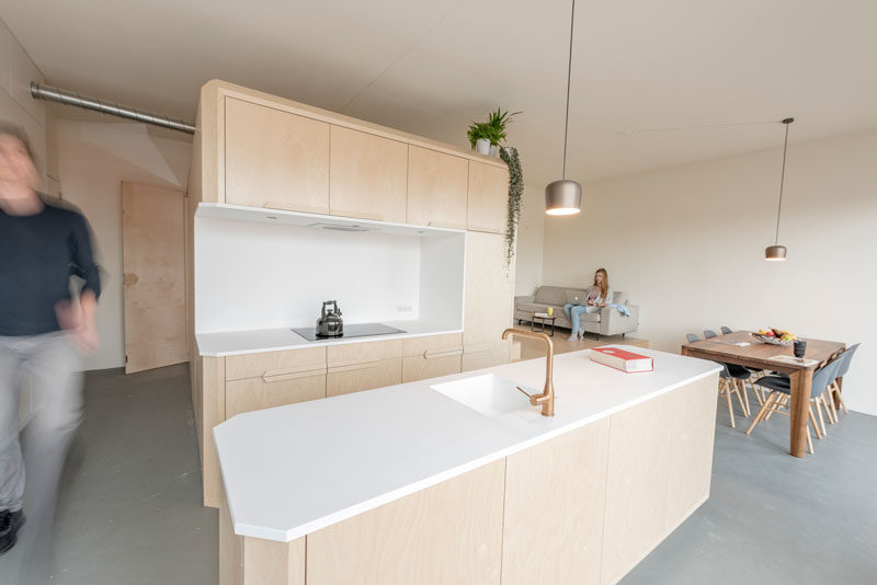 This modern loft apartment has a subtle palette of birch wood and white Corian. There's a bathroom, storage room, kitchen, raised living room, and a lofted bedroom. #InteriorDesign #ApartmentDesign #Loft