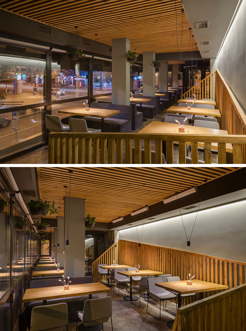 In this modern restaurant, large windows provide a street view for the diners, while behind them, an angled wood slat detail breaks up the grey wall. #RestaurantDesign #InteriorDesign