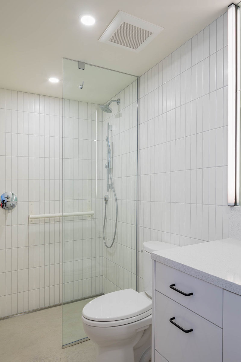 This white bathroom features a walk-in shower with a glass shower green, and rectangular white tiles in a vertical orientation. #WhiteBathroom