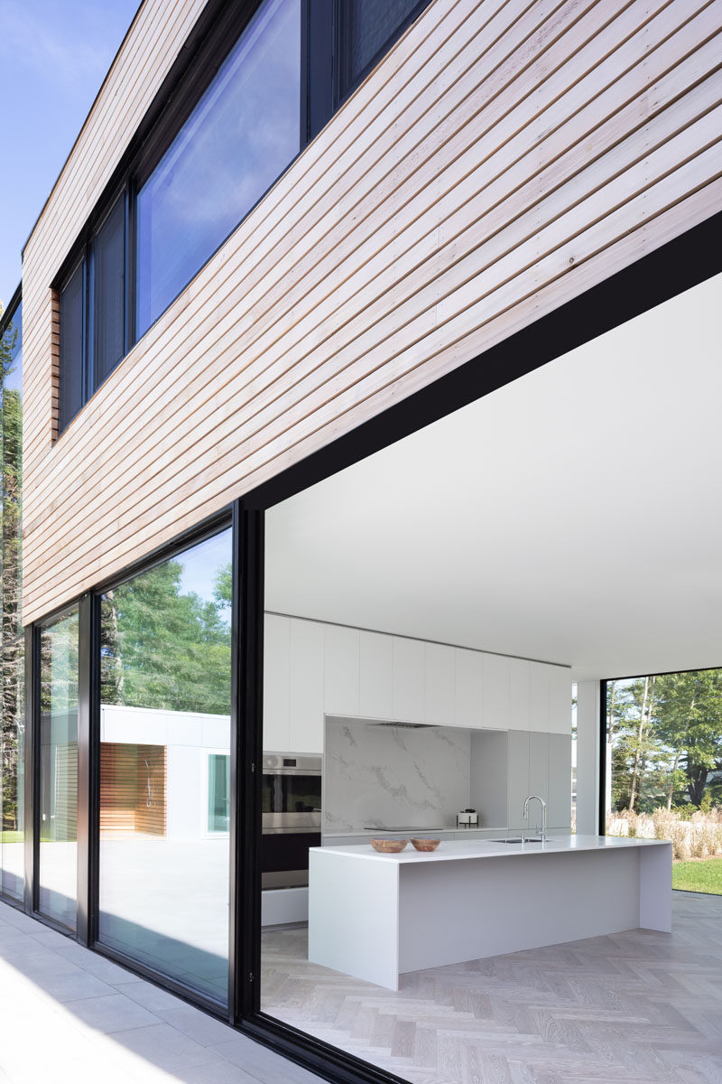 Throughout this modern house herringbone patterned white oak floors cover the floor, while minimalist white cabinets have been used in the kitchen. #HerringboneFlooring #WhiteKitchen #KitchenDesign