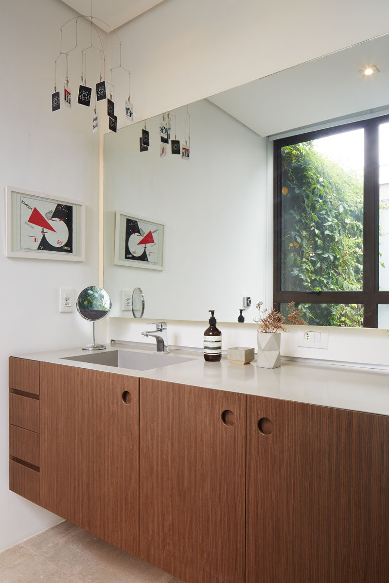 In this modern bathroom, there's a wood vanity with a light colored countertop, and a large mirror reflects a green wall outside. #BathroomDesign #ModernBathroom #WoodBathroomVanity