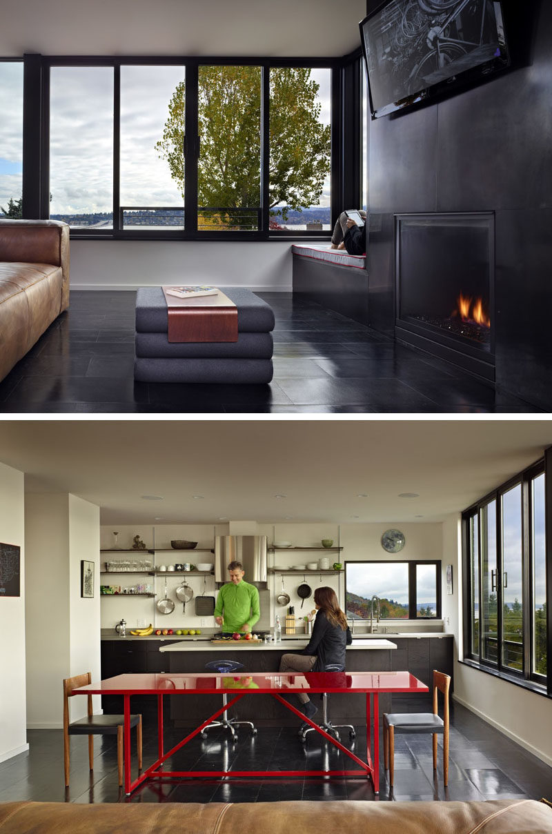 The social areas of this modern house are open plan, with the living room, dining, and kitchen all enjoying the views from the windows that line the wall. Beside the fireplace in the living room, there's built-in window seat with an upholstered cushion. #OpenPlanInterior #Fireplace #WindowSeat #Kitchen