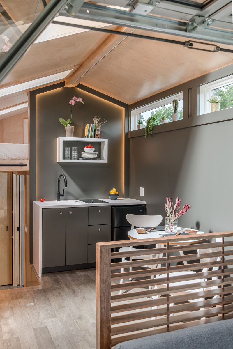 In the kitchen of this tiny house, there's a small sink, cooktop, fridge and small amount of storage. Hidden lighting gives the kitchen a soft glow. #TinyHouse #TinyHome #TinyKitchen