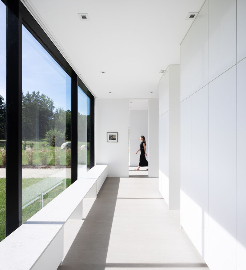 This modern hallway is lined with storage closets and benches positioned beside the floor-to-ceiling windows. #Hallway #ModernInterior #GlassWall