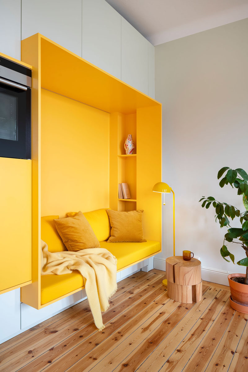 This renovated 1920s apartment in Stockholm received a modern makeover, with a custom designed wall that includes yellow built-in sections that house a kitchen and a seating nook. #InteriorDesign #Kitchen #SeatingNook