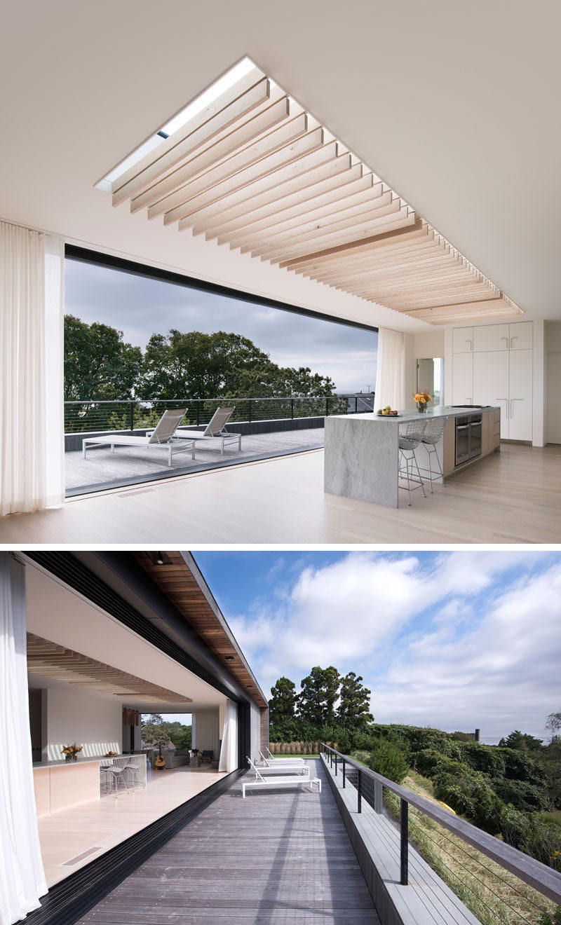 A large retracting glass wall connects the interior of this modern house with the outdoor spaces, enabling ocean views, breezes, and natural lighting to filter through. #ModernHouse #Skylight #InteriorDesign