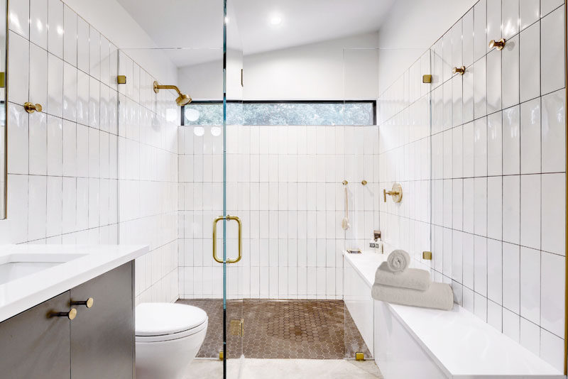 In this modern bathroom, white glossy tiles cover the walls, while a glass shower screen allows natural light from the window to filter through to the rest of the bathroom. #Bathroom #ModernBathroom #BathroomDesign