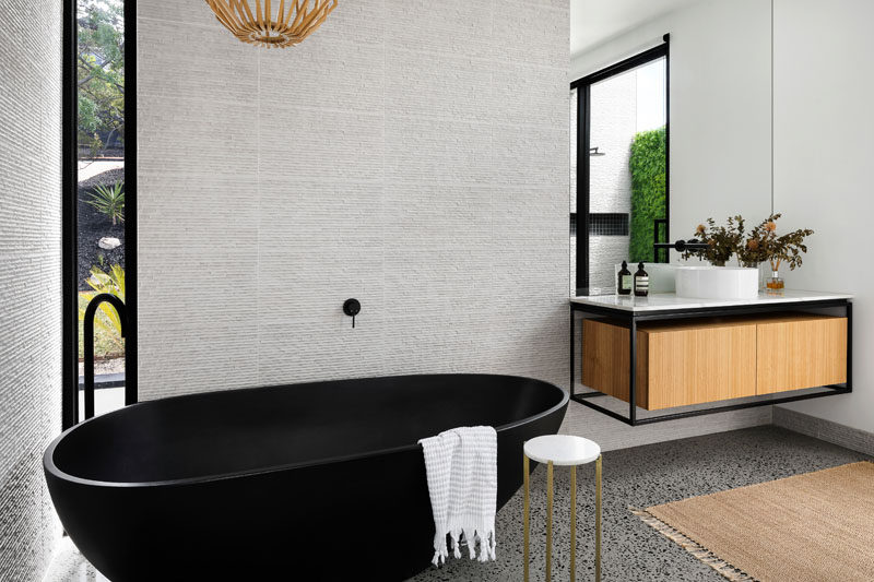 In this modern bathroom, a matte black freestanding bathtub complements the black detailing on the vanity and the window frames. #ModernBathroom #BlackBathtub #InteriorDesign