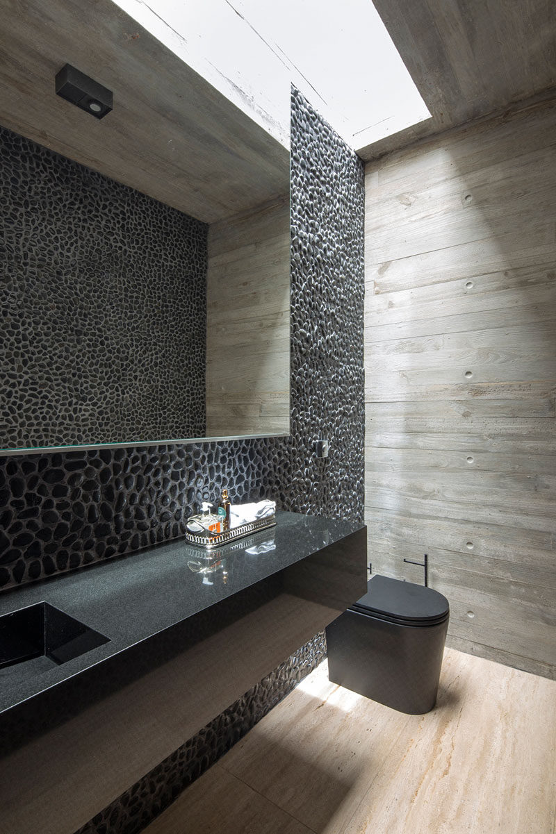 In this modern master bedroom, a feature wall of pebbles with a mirror reflects the pebbles on the opposite wall, while a skylight provides extra light to the room. #ModernBathroom #BathroomDesign