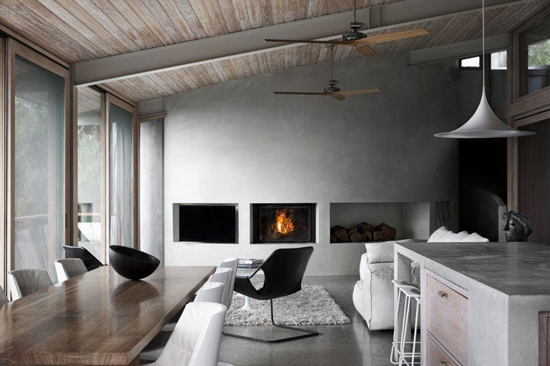 In this modern living room, a curved concrete wall has built-in areas for a television, fireplace, and wood storage. #LivingRoom #CurvedConcreteWall #Fireplace