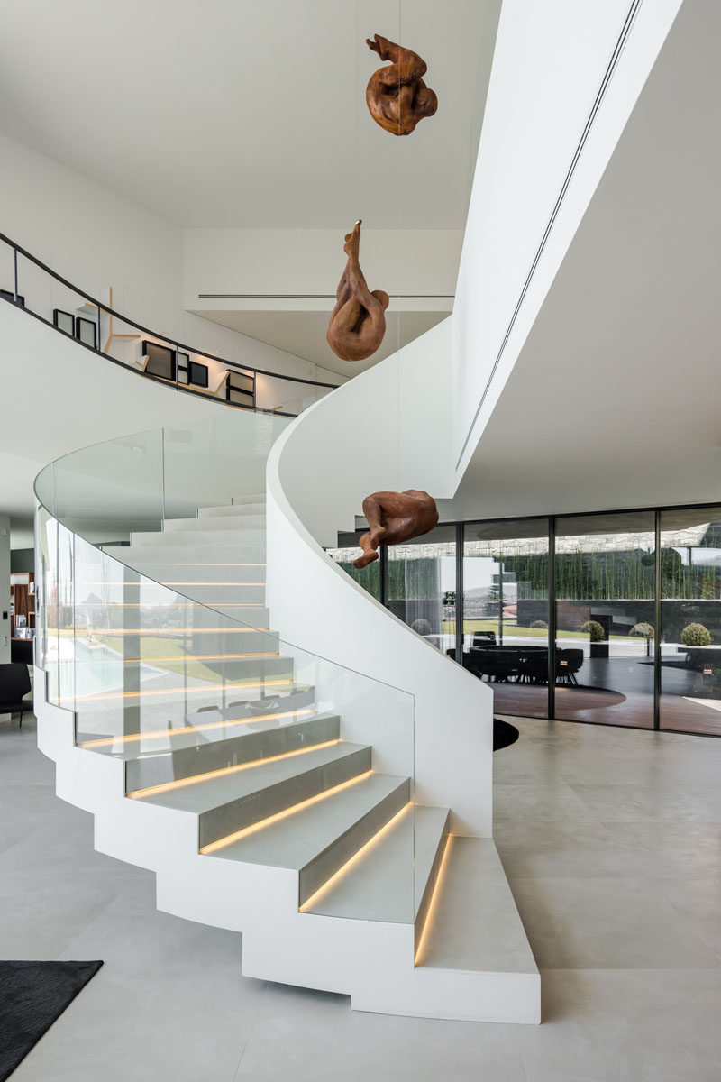 A curved white staircase with glass handrails and hidden lighting connects the various levels of this modern house. #Staircase #Stairs #CurvedStairs #ModernStairs