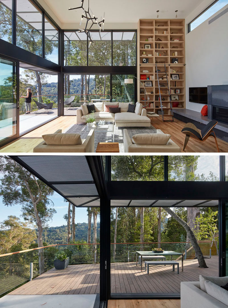 In this modern living room, double height ceilings make the living room feel large and open, with walls of windows showing off the views, while a floor-to-ceiling wood bookcase provides a place to display personal items. #LivingRoom #Shelving #GlassWalls