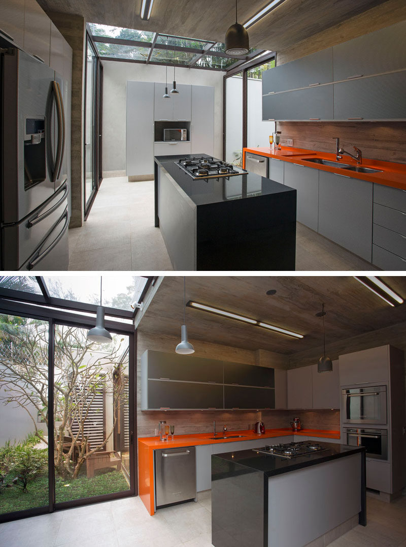 In this modern kitchen, a section of the ceiling has been made from glass, allowing for natural light to filter through, while a sliding glass door opens up to a small courtyard with seating. #ModernKitchen #KitchenDesign