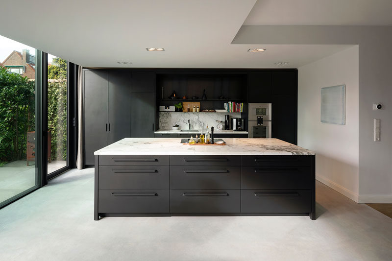 A new kitchen was created inside this modern house extension, and the dark cabinetry is a strong contrast to the white walls, ceiling, and light concrete floor. #ModernKitchen #DarkCabinetry #DarkKitchen #ConcreteFloors