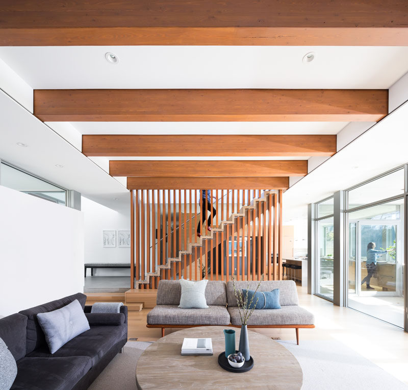 The living room in this modern house has a ceiling that's composed of exposed 5"x12" stained Douglas Fir glulam beams that extend outward to create a covered patio deck. #Ceiling #Beams #WoodBeams #LivinRoom