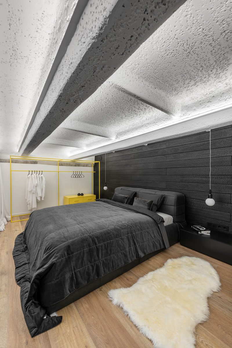 In this modern loft bedroom, soft white curtains can be closed for privacy, while the contrasting accent wall behind the bed is covered by burnt Accoya wood. A pop of yellow has also been added in the form of a freestanding open closet. #ModernBedroom #BlackAccentwall #BurntWoodWall