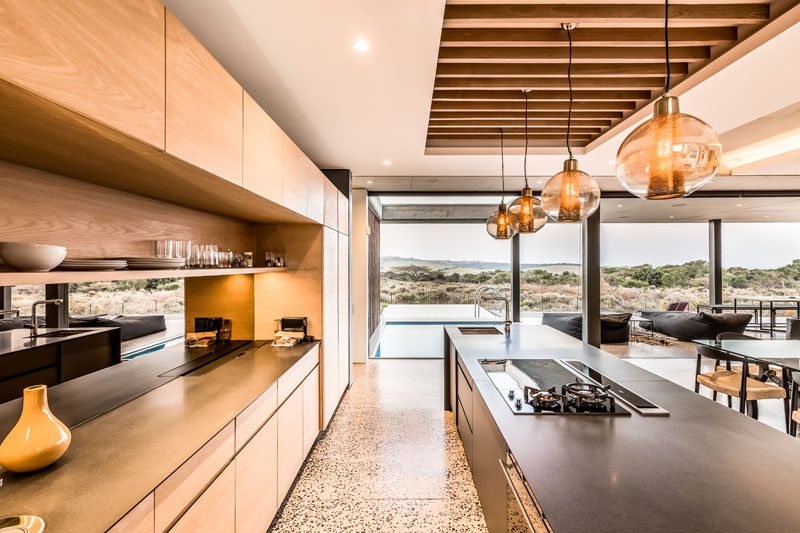 The long kitchen island draws your eye towards the swimming pool outside. #ModernKitchen #KitchenDesign #WoodCabinets