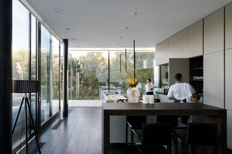 The glass corner windows in this modern kitchen give the feeling of living on the water, and large trees nearby provide privacy for the occupants. #Windows #KitchenDesign #InteriorDesign