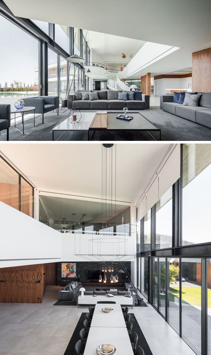 Inside this modern house, the living room, with a grey accent wall and dark grey furniture, is located at one end of the home. Large sliding glass doors open the interior to the outdoor patio and swimming pool. #LivingRoom #OpenPlanInterior #ModernInterior