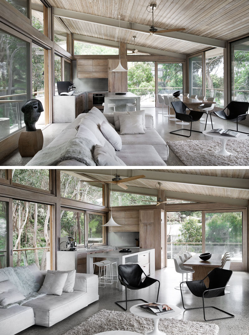 The living room of this modern house opens to the open plan dining room and kitchen. A sloped wood adds a natural warmth to the interior, while floor-to-ceiling windows capture the view of the surrounding trees. #ModernInteriorDesign #WoodCeiling #ConcreteKitchen