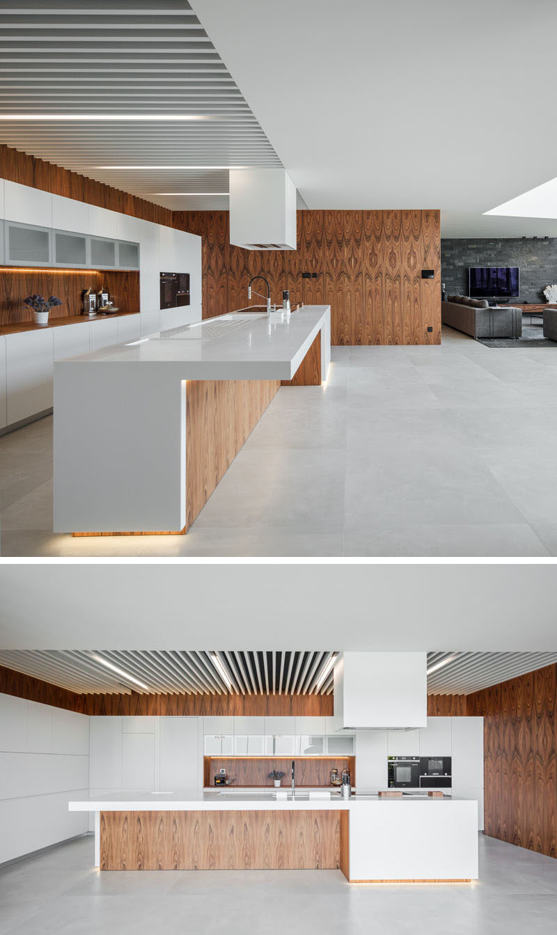 The open plan interior of this modern house allows for easy movement between the different social areas of the house, while the kitchen is defined by the use of wood walls that provide a backdrop for the white cabinets. #ModernKitchen #WoodAndWhiteKitchen #KitchenDesign