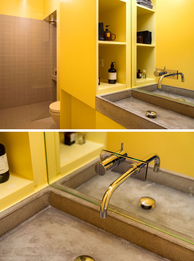 This modern bathroom features yellow walls and cabinetry, and a concrete sink. #BathroomDesign #YellowBathroom