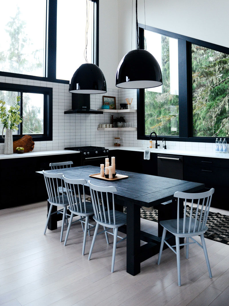 In this contemporary kitchen, lower black cabinets tie in with the black dining table, while white tiles and open corner shelving has been installed on the walls. #KitchenDesign #BlackAndWhiteKitchen