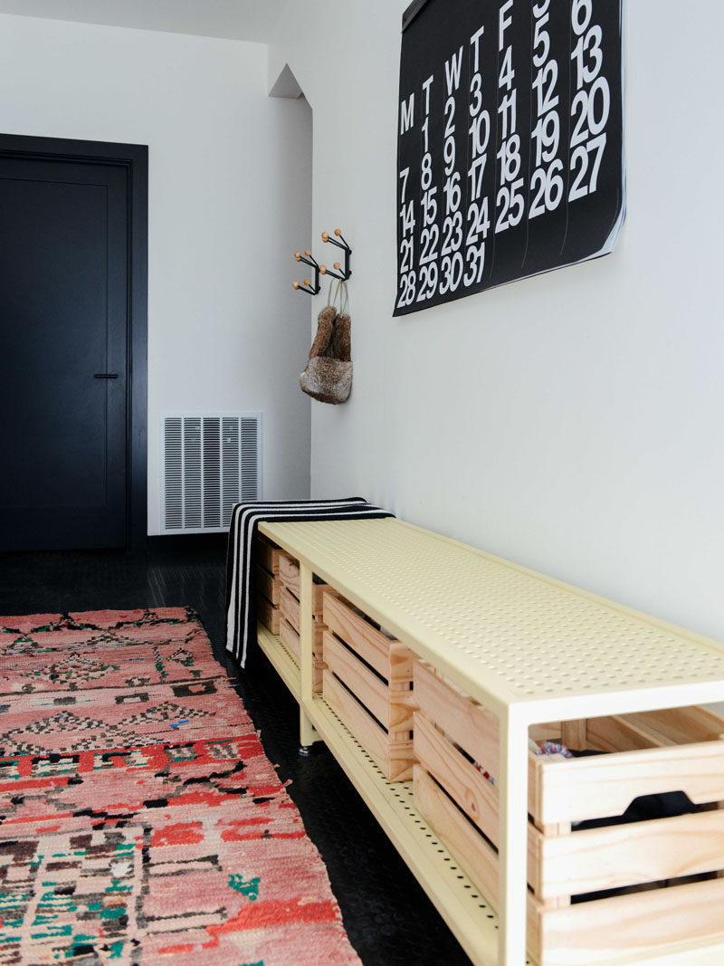 A colourful rug adds warmth to this contemporary entryway that features black flooring and a steel bench with wood cubbies. #Entryway #InteriorDesign