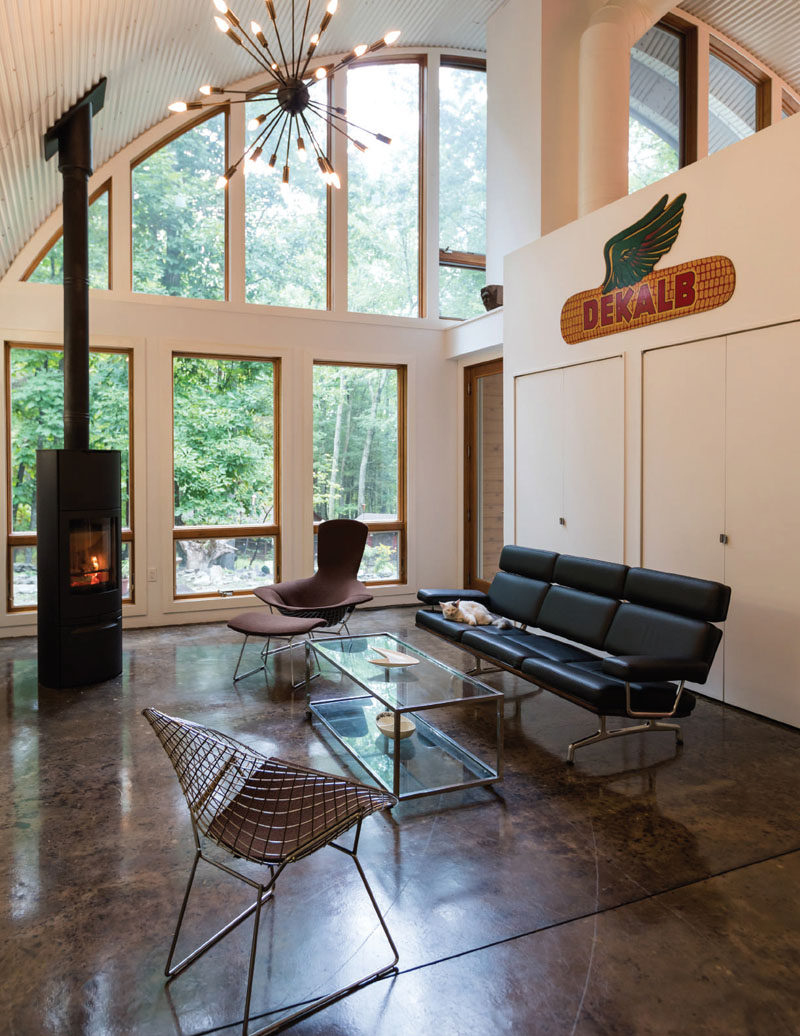 The interior of this modern house is bright and open, with high ceilings and plenty of windows. In the living room, there's a fireplace for cool nights, and sculptural pendant light hanging from the ceiling adds an artistic flair to the space. #ModernHouse #LivingRoom #Fireplace #ConcreteFlooring